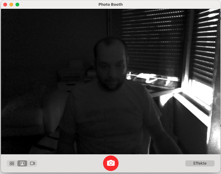 Screenshot von PhotoBooth mit einem seltsamen schwarz-weiß Bild. Die Farben werden nicht korrekt wiedergegeben. Man kann schemenhaft eine Person erkennen, die an einem Computer sitzt.